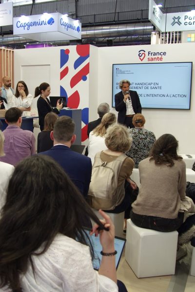 Vincent Julé intervient au micro sur le stand France Santé d’un salon professionnel, devant un public assis, à côté d’un écran du ministère de la Santé titré « Référent handicap en établissement de santé : de l’intention à l’action ».